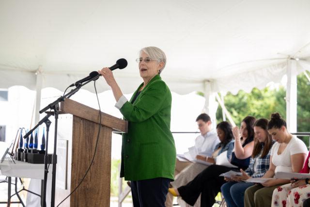 Woman with gray hair and in a green suit standing at a podium